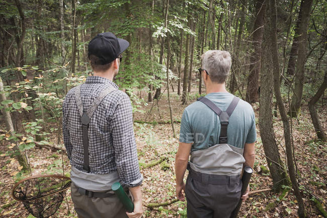 Vista trasera de dos hombres con equipo de pesca con mosca en la zona forestal . - foto de stock