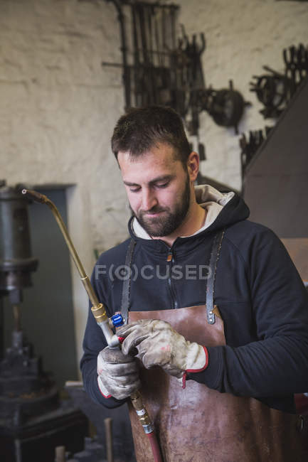 Un forgeron dans un tablier de cuir utilise une torche de coupe dans son atelier
. — Photo de stock