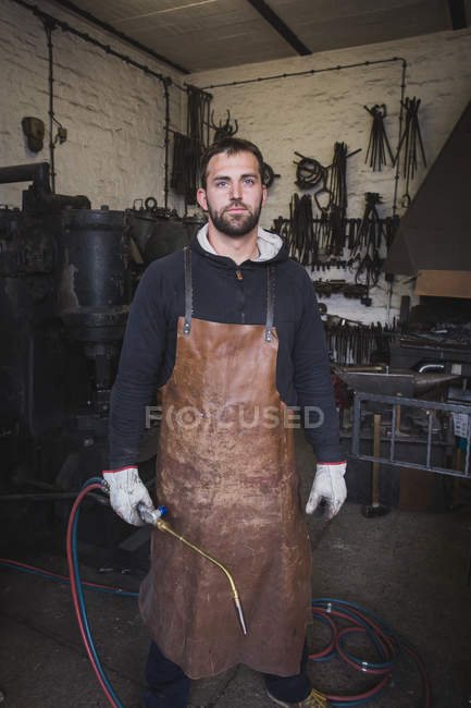 A blacksmith in a leather apron and with a cutting torch is portrayed in his workshop. — Stock Photo
