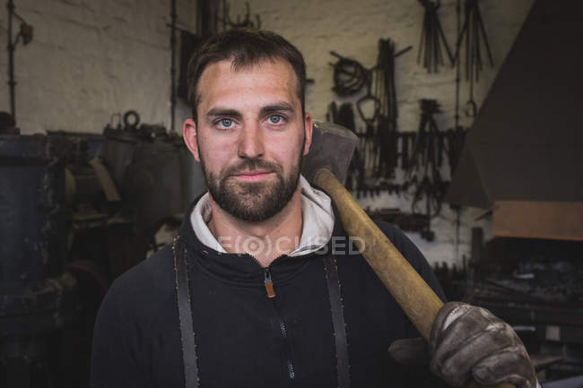 A blacksmith in a leather apron and with a sledgehammer is portrayed in his workshop. — Stock Photo