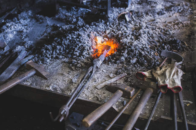 Um ferreiro está aquecendo uma barra de ferro em uma oficina . — Fotografia de Stock