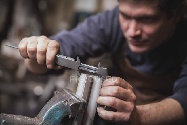 A blacksmith is taking measures on a piece of metal in a workshop. — Stock Photo