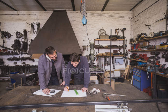 Dois ferreiros estão tomando medidas, fazendo cálculos e agendando um dia de trabalho na oficina de um ferreiro . — Fotografia de Stock