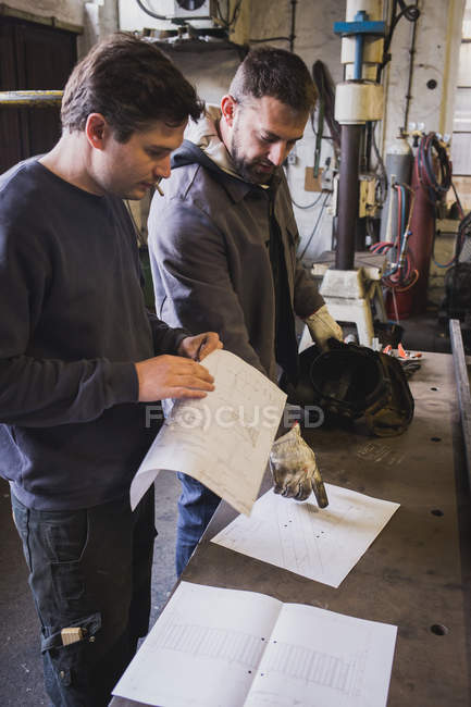 Two blacksmiths are taking measures, do calculations and schedule a days work in a blacksmith's workshop. — Stock Photo