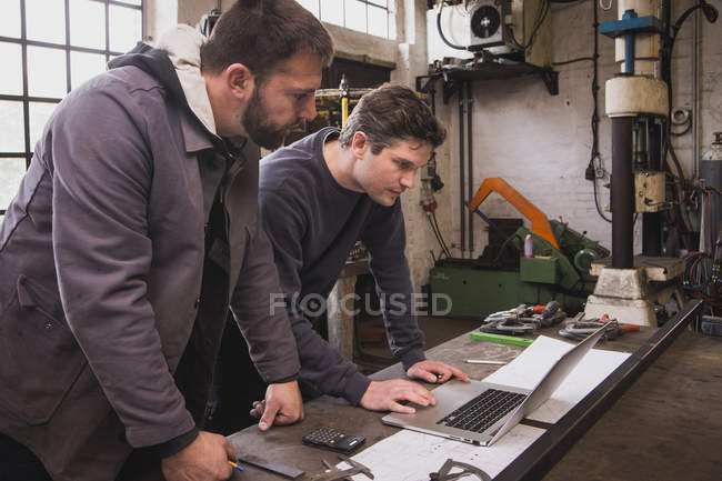 Dos herreros están tomando medidas, haciendo cálculos y programando un día de trabajo en la computadora en el taller de un herrero
. - foto de stock
