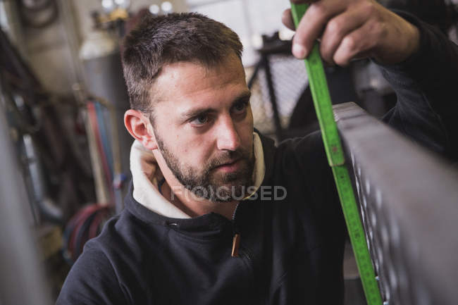 Un fabbro sta prendendo misure su un pezzo di metallo in un laboratorio . — Foto stock