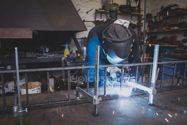 Un forgeron porte un équipement de sécurité et soude une construction métallique dans un atelier de métallurgie
. — Photo de stock