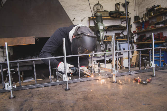 Um ferreiro usa engrenagem de segurança e está soldando uma construção de metal na oficina de um metaleiro
. — Fotografia de Stock