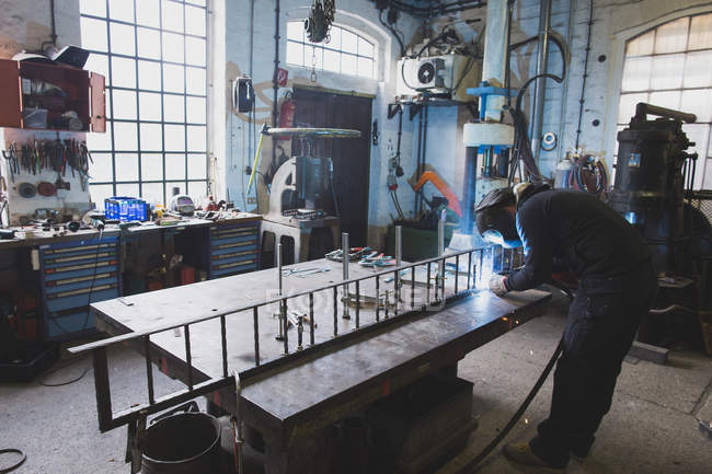 Um ferreiro usa engrenagem de segurança e está soldando uma construção de metal na oficina de um metaleiro . — Fotografia de Stock