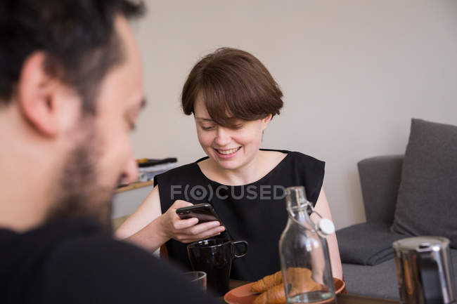 Young woman is checking her smart phone during breakfast with her boyfriend. — Stock Photo