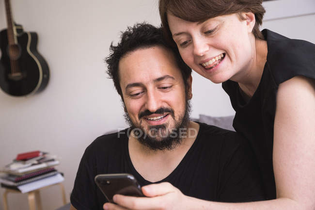 Jeune femme vérifie son téléphone intelligent pendant le petit déjeuner et partage des nouvelles avec son petit ami . — Photo de stock