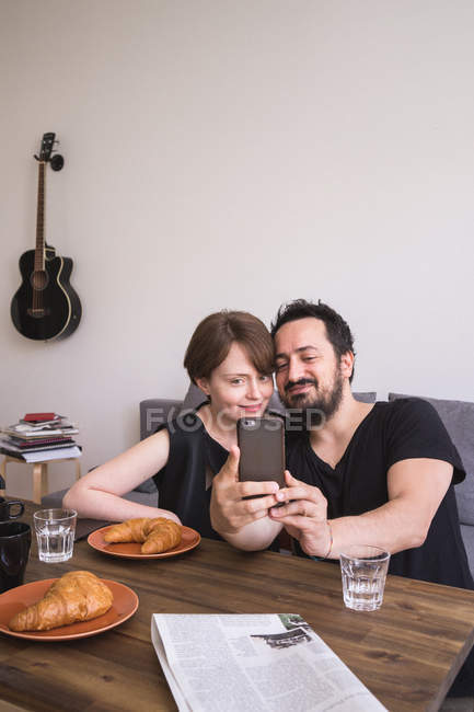 A young couple is doing selfies with a smart phone at the breakfast table. — Stock Photo