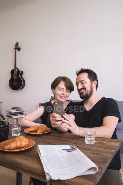 Una pareja joven está haciendo selfies con un teléfono inteligente en la mesa del desayuno . - foto de stock