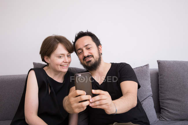 A young couple is doing selfies with a smart phone while chilling out on the couch during weekend. — Stock Photo