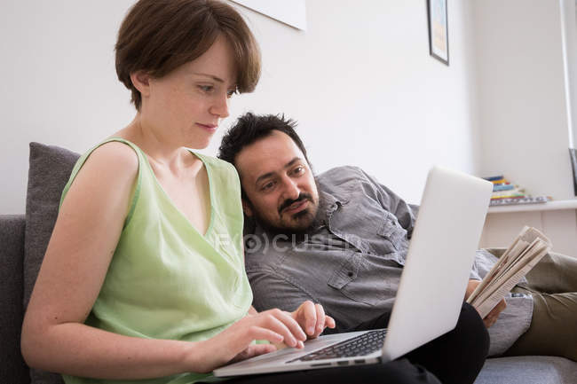 Молода жінка на комп'ютері у вітальні з хлопцем, лежачи на дивані. — стокове фото