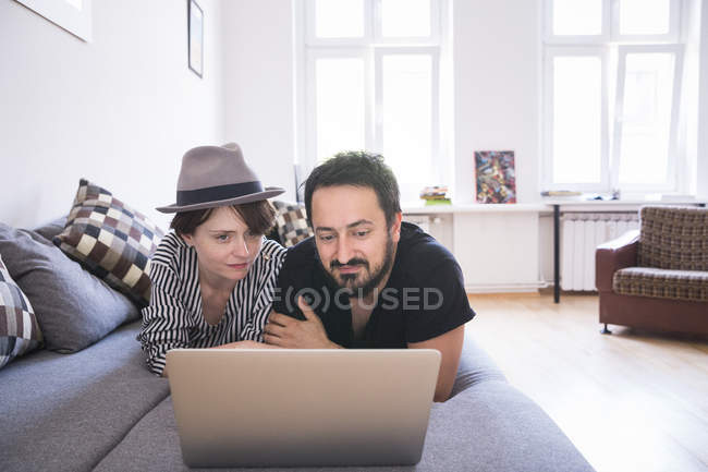 Una joven pareja está navegando por Internet mientras se relaja en el sofá de la sala de estar . - foto de stock