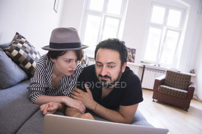 Um jovem casal está navegando na Internet enquanto relaxa no sofá na sala de estar . — Fotografia de Stock