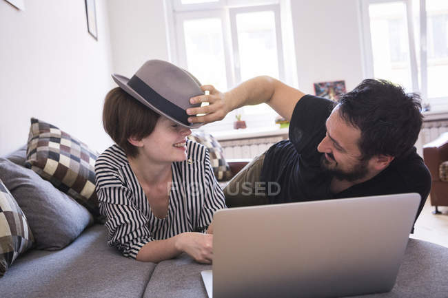 Un jeune couple diffuse des séries télévisées sur l'ordinateur tout en s'amusant sur le canapé dans le salon . — Photo de stock