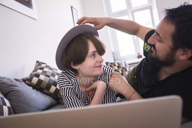 Una joven pareja está transmitiendo series de televisión en el ordenador mientras se relaja en el sofá de la sala de estar
. - foto de stock