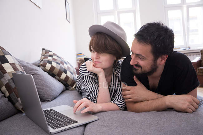 Um jovem casal está transmitindo séries de TV no computador enquanto relaxa no sofá na sala de estar
. — Fotografia de Stock