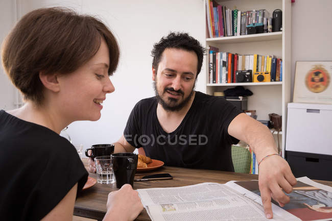 A young couple read newspaper at the breakfast table during a weekend at home. — Stock Photo