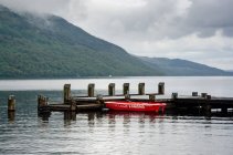 Reino Unido, Escocia, Argyll y Bute, Arrochar, barco amarrado por muelle de madera en el lago Loch Lomond - foto de stock