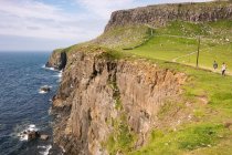 Reino Unido, Escocia, Highland, Isla de Skye, Glendale, Gente caminando por los acantilados verdes de Neist Point junto al mar - foto de stock