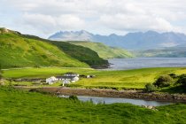 Reino Unido, Escocia, Highland, Isla de Skye, Vista de la bahía de Gesto, Paisaje natural verde con pueblo junto al lago de montaña - foto de stock