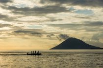 Indonesia, Sulawesi Utara, Kota Manado, gente en un barco en Sulawesi Utara en susnet, montaña en el fondo - foto de stock