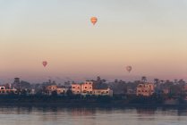 Дальний вид на дома вблизи реки и воздушных шаров, Луксор, Луксор провинции, Египет — стоковое фото