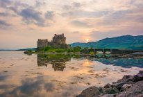 Reino Unido, Escocia, Highland, Dornie, Loch Duich, Eilean Donan Castle by lake at scenic sunset - foto de stock