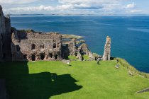Великобритания, Шотландия, Ист-Лотиан, Северный Бервик, Замок Танталлон руины зеленого Фесси Медоу у моря — стоковое фото