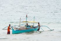 Indonesia, Maluku Utara, Kabul Pulau Morotai, hombres con barco en el mar en la tierra Pandanga en el norte de Molikken - foto de stock