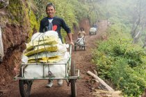 JAVA, INDONESIA - 18 DE JUNIO DE 2018: Trabajadores que transportan azufre del volcán Ijen en carruajes - foto de stock