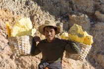 JAVA, INDONESIA - 18 GIUGNO 2018: Estrazione di zolfo sul vulcano Ijen, uomo che trasporta zolfo nei cestini dal cratere — Foto stock