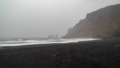 Schwarzer Sandstrand mit nebelbedeckten Felsen, Island, Myrdalshreppur — Stockfoto