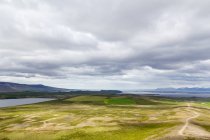 Campos verdes y montañas lejanas bajo el cielo nublado, Islandia - foto de stock