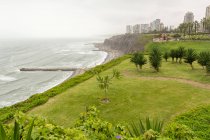 Peru, provincia de lima, miraflores, grüne Meeresküste mit Lima Stadtbild im Hintergrund im Nebel — Stockfoto