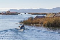 Perú, Puno, Puno, hombre en barco en el lago Titikaka Isla de los Uros vista pequeña aldea - foto de stock