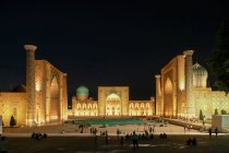 Узбекистан, Самарканд, Самарканд, люди, идущие по площади возле медресе, освещенные ночью — стоковое фото