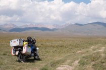 Kirguistán, región de Naryn, distrito de Kochkor, motocicleta estacionada en el campo - foto de stock