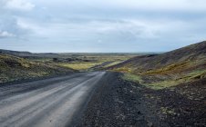 Feldweg mit ferner Landschaft unter wolkenverhangenem Himmel, Island — Stockfoto