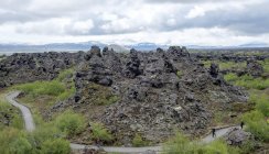 Touristes lointains et structures de lave sous un ciel nuageux, Islande, Dimmuborgir — Photo de stock