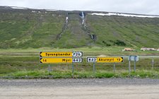 Sinais de direção amarela com colina verde no fundo, Islândia — Fotografia de Stock