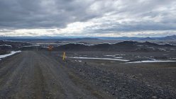 Estrada de terra com montanhas distantes sob céu nublado, Islândia — Fotografia de Stock