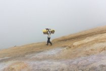 JAVA, INDONÉSIA - 18 DE JUNHO DE 2018: Mineração de enxofre no vulcão Ijen, homem transportando enxofre em cestas por cratera — Fotografia de Stock