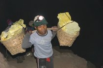 JAVA, INDONESIA - JUNE 18, 2018: Sulfur mining on the volcano Ijen, man carrying baskets with sulfur in early morning — Stock Photo