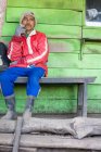 JAVA, INDONESIA - JUNE 18, 2018: worker resting by wooden hut, sitting on bench and smoking — Stock Photo