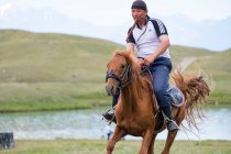 REGIONE OSH, KIRGYZSTAN - LUGLIO 22, 2017: Uomo a cavallo hore, paesaggio montano con lago sullo sfondo — Foto stock