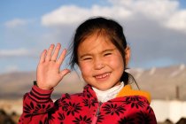Chica asiática sonriendo saludando con la mano a la cámara, Tayikistán - foto de stock